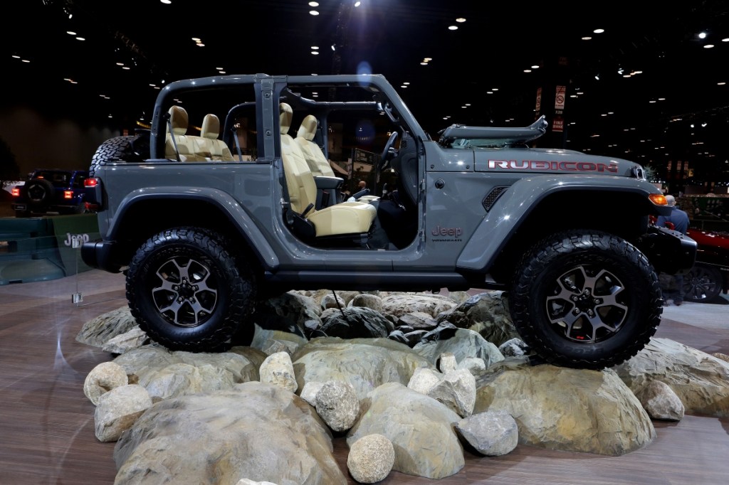 A gray, two door Jeep Wrangler sits atop rocks while on display at a car show.
