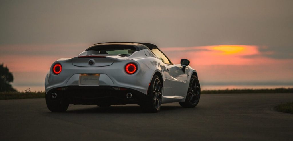 The rear of a white Alfa Romeo 4C convertible sits on the coast at sunset.