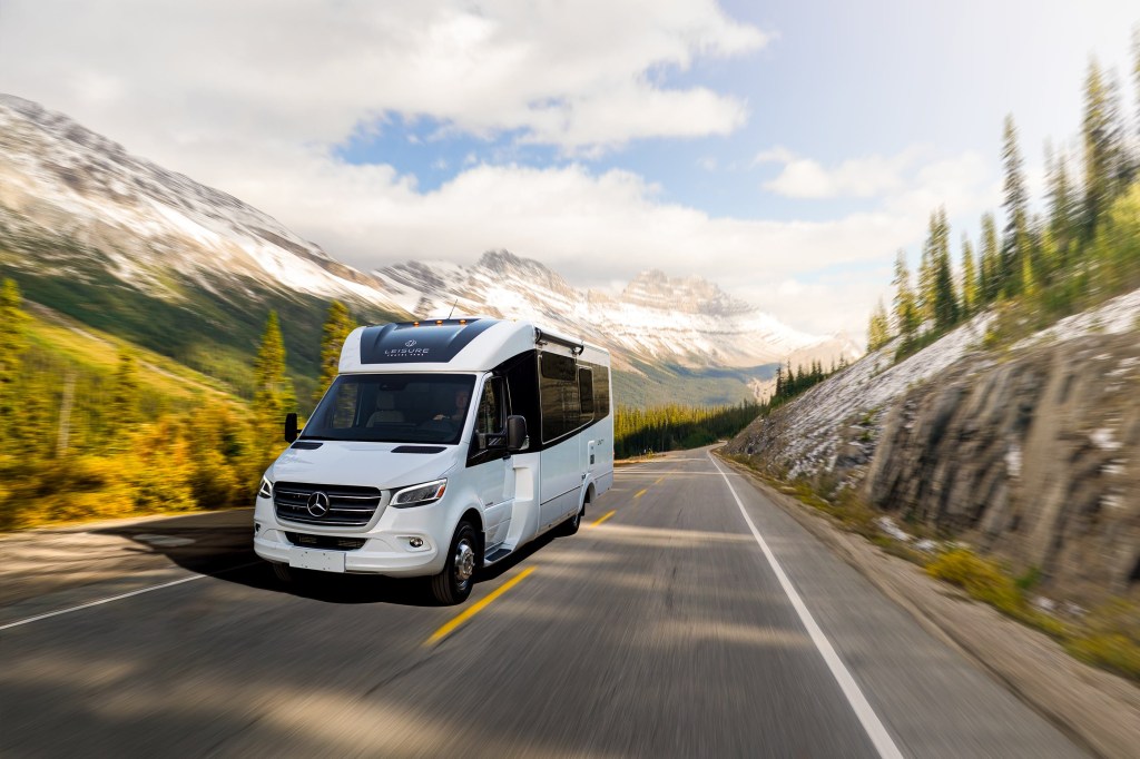 White 2020 Leisure Travel Vans Unity RV driving through a forested mountain road