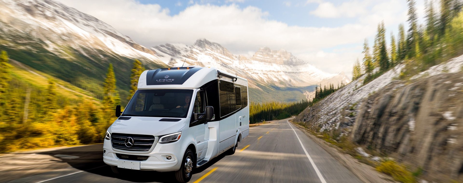 White 2020 Leisure Travel Vans Unity RV driving through a forested mountain road