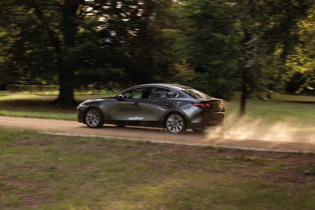 a gray Mazda3 Sedan in motion on a scenic dirt road is a newer model without current complaints
