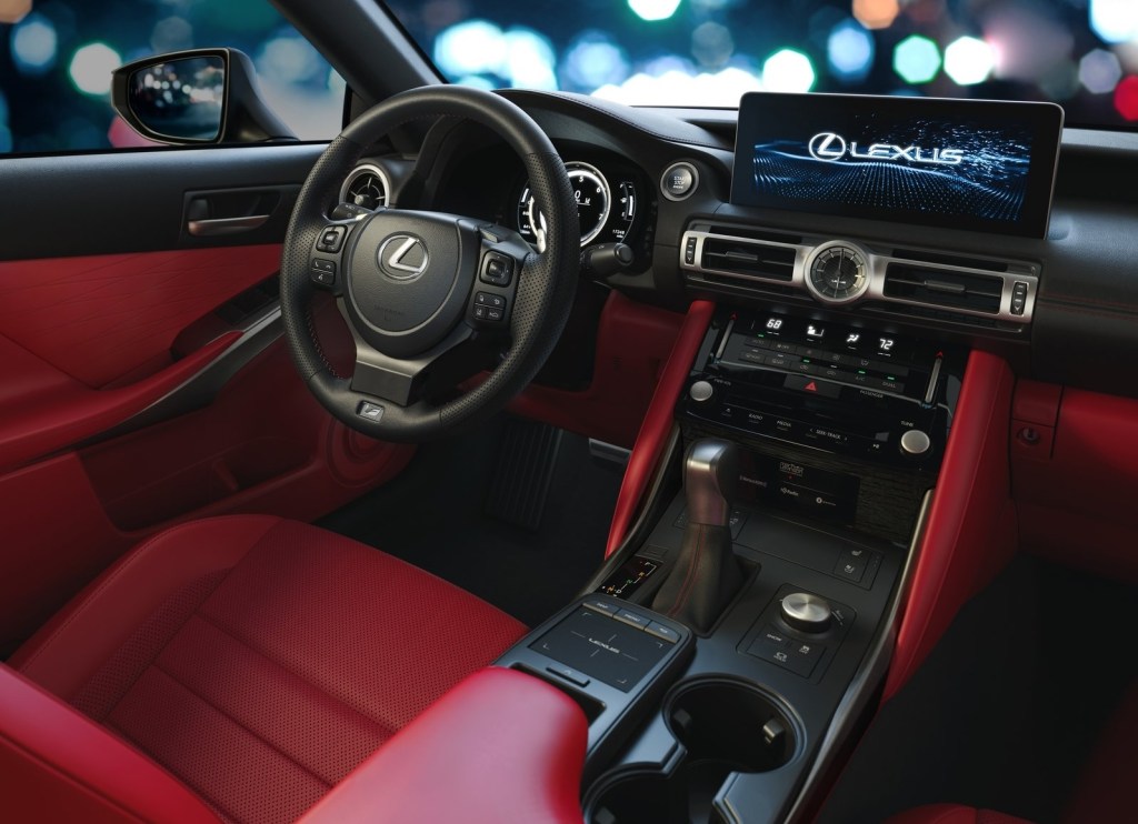 The 2021 Lexus IS 350 F Sport's interior, showing the red upholstery and center console trim, touchscreen, touchpad, and digital instrument cluster