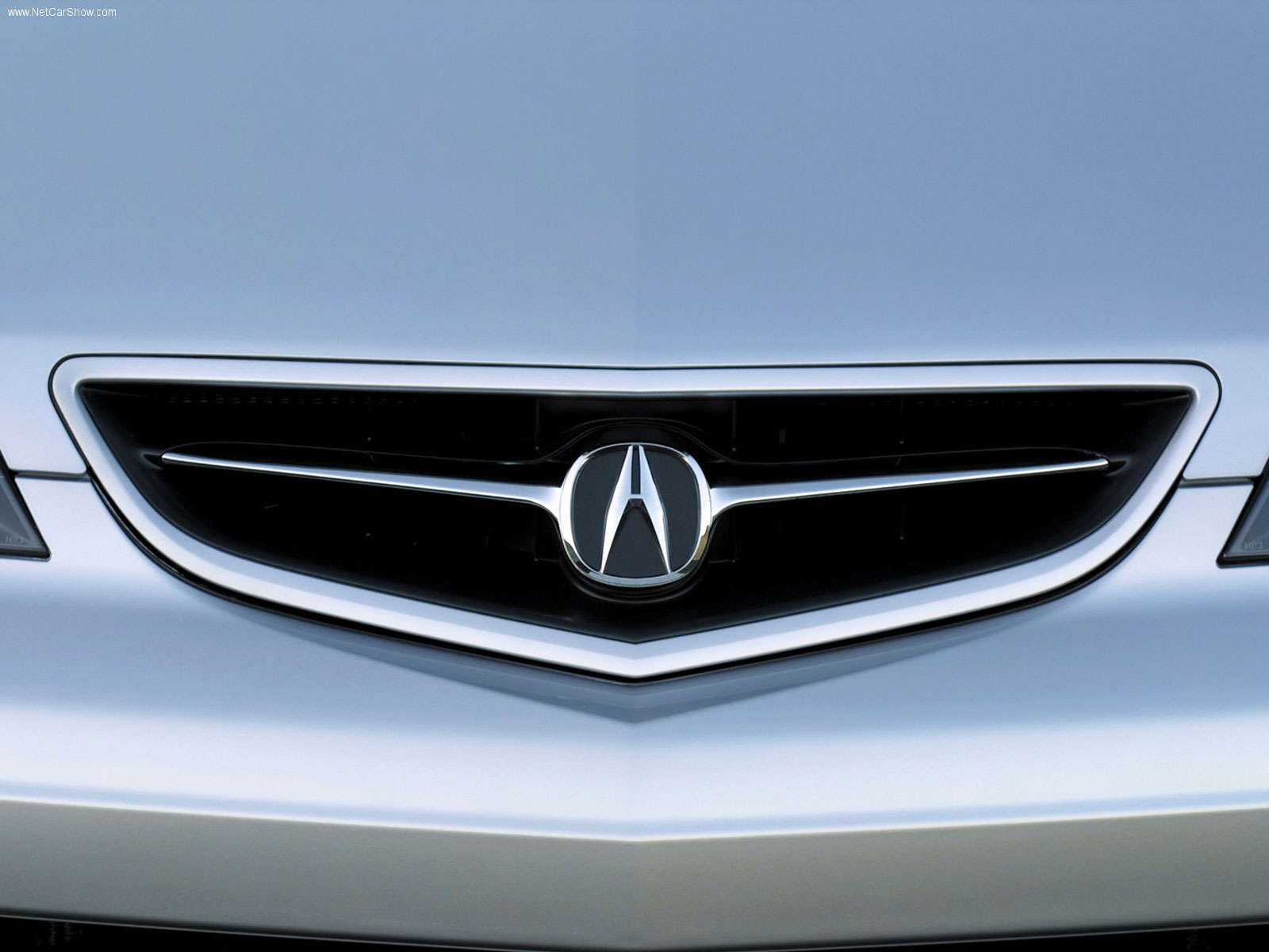 The shining chrome Acura badge sits in the middle of the grille of a silver car.