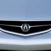 The shining chrome Acura badge sits in the middle of the grille of a silver car.