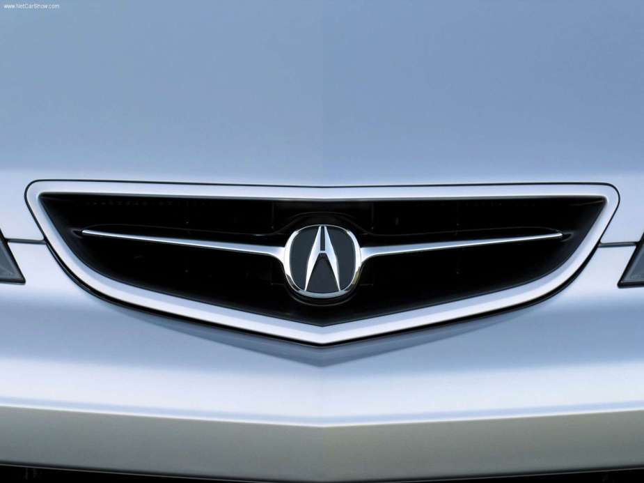 The shining chrome Acura badge sits in the middle of the grille of a silver car.