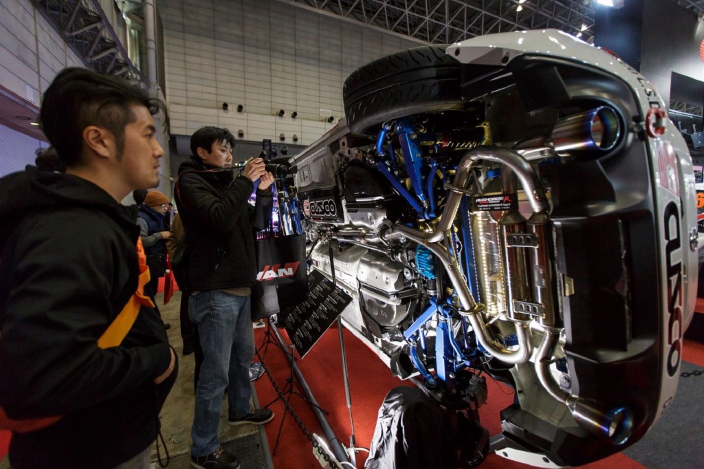 Visitors look at the aftermarket exhaust of a sideways-turned car