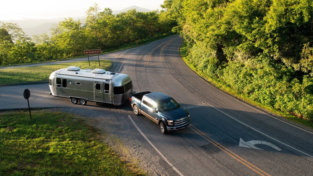 Silver Airstream Flying Cloud camper being towed by a blue Ford F-150 in a forested national park
