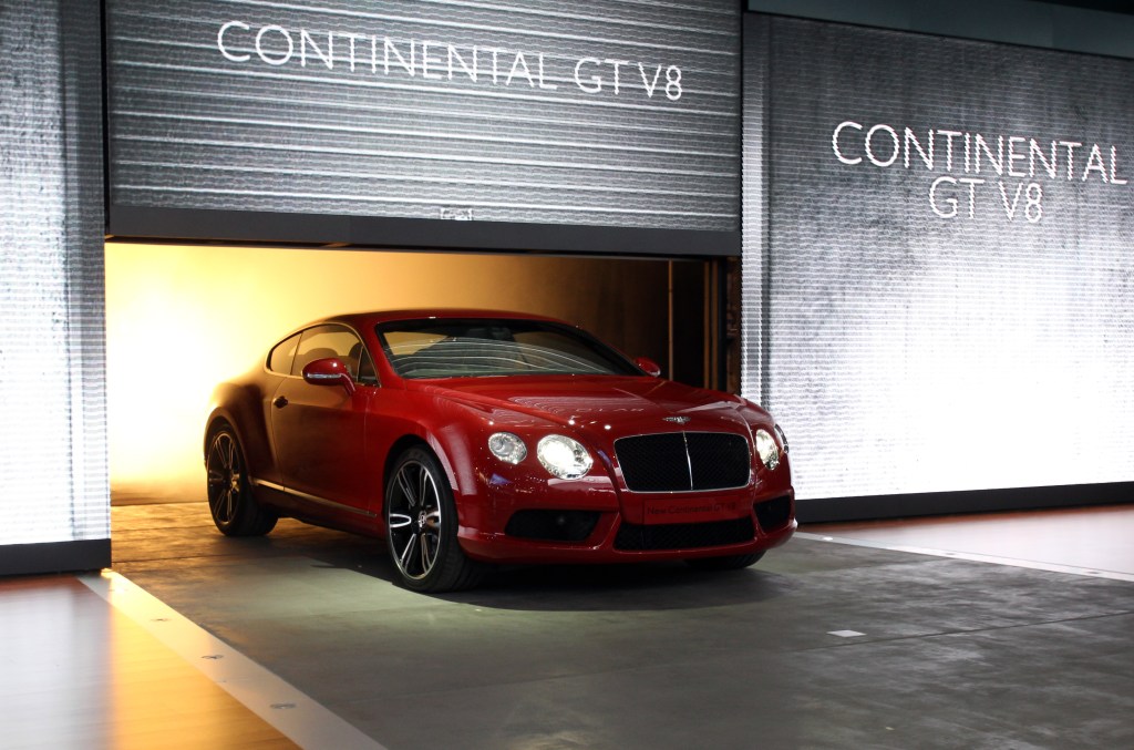 A red Bentley Continental GT V8 pulls under a backlit garage door