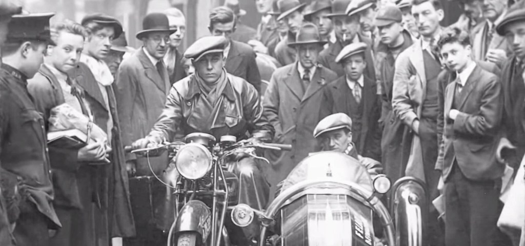 Black-and-white shot of Carlo Abarth seated on his motorcycle, with his co-driver in the sidecar, in front of a large crowd