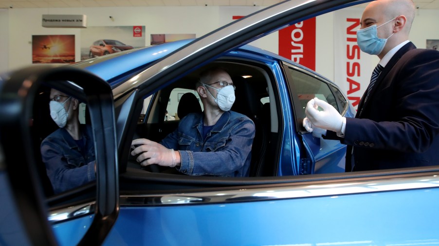 A customer and dealership employee with masks discuss a car in a showroom.