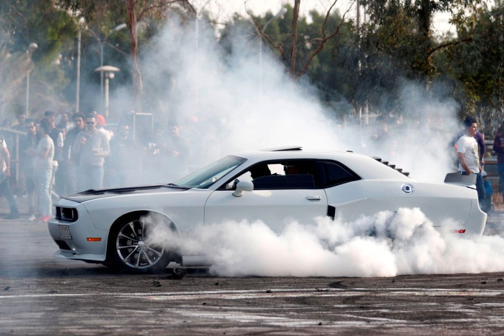 The driver of a white Dodge Challenger performs a burnout