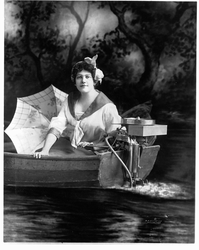 Early 1900s woman in boat posing with new Evinrude engine