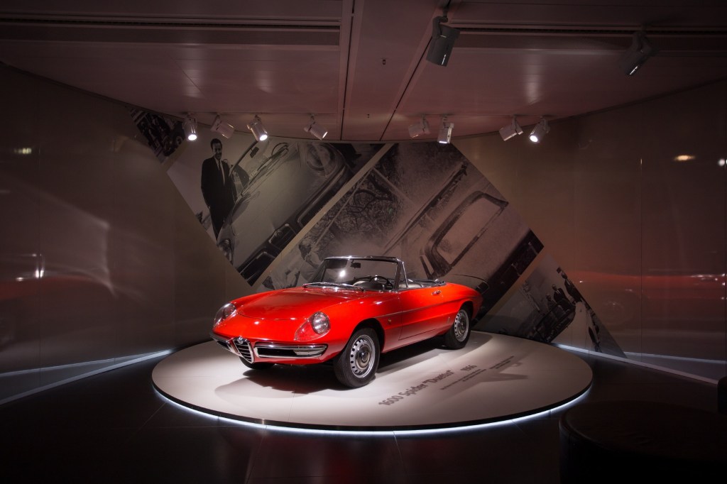A red Alfa Romeo Spider from 1966 sites on a turntable in a museum.