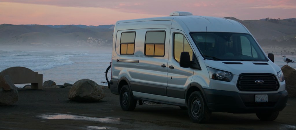 A Ford Transit van that has been converted for vanlife sits by the beach.