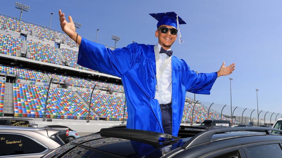 A high school senior in cap and gown arrives at his graduation at Daytona International Speedway