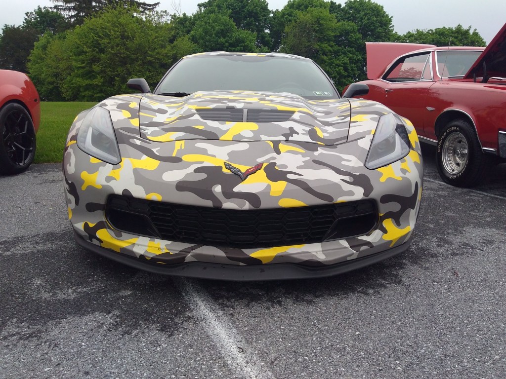 The front end of a C7 Corvette that has been wrapped in a grey and yellow camouflage.