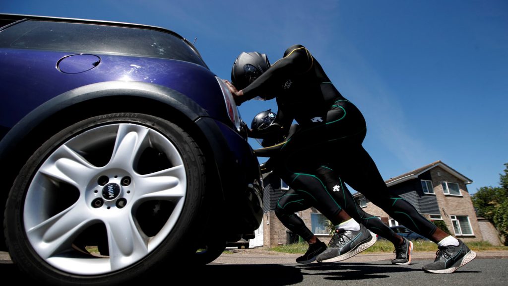Two team members in team uniform push a blue Mini Cooper