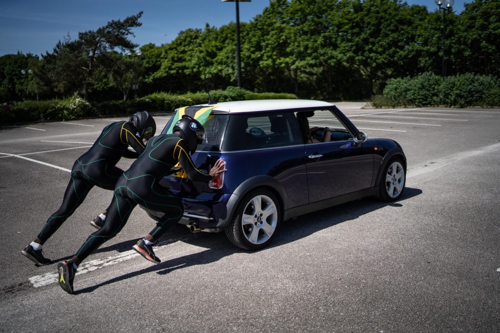 Two team members in team uniform push a blue Mini Cooper through a parking lot.