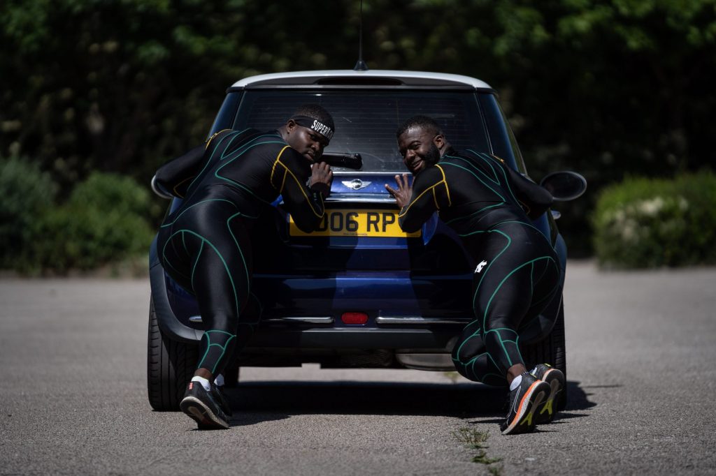Two team members in team uniform push a blue Mini Cooper