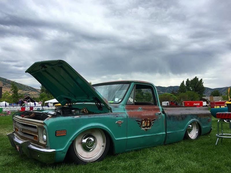 a rusty vintage Chevy C-10 Pickup truck parked in the grass with the hood open