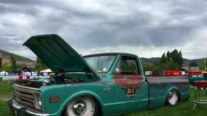 a rusty vintage Chevy C-10 Pickup truck parked in the grass with the hood open