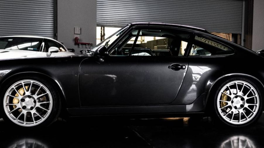 A black Porsche 964 sits in an indoor parking lot.