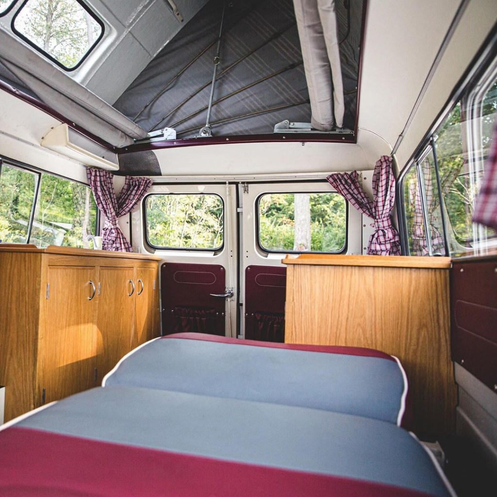 The restored interior of a 1961 Bedford CA Dormobile, showing the wood-paneled fridge, sink, and stove, and pop-up tent