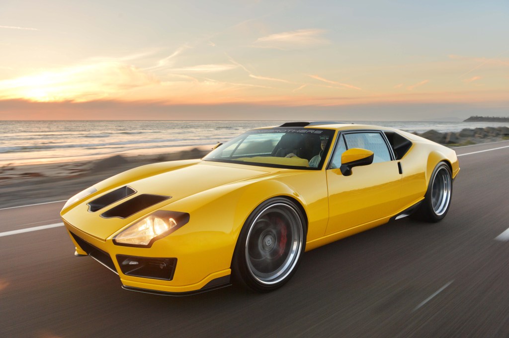 A yellow custom DeTomaso Pantera driving down a coastal road.