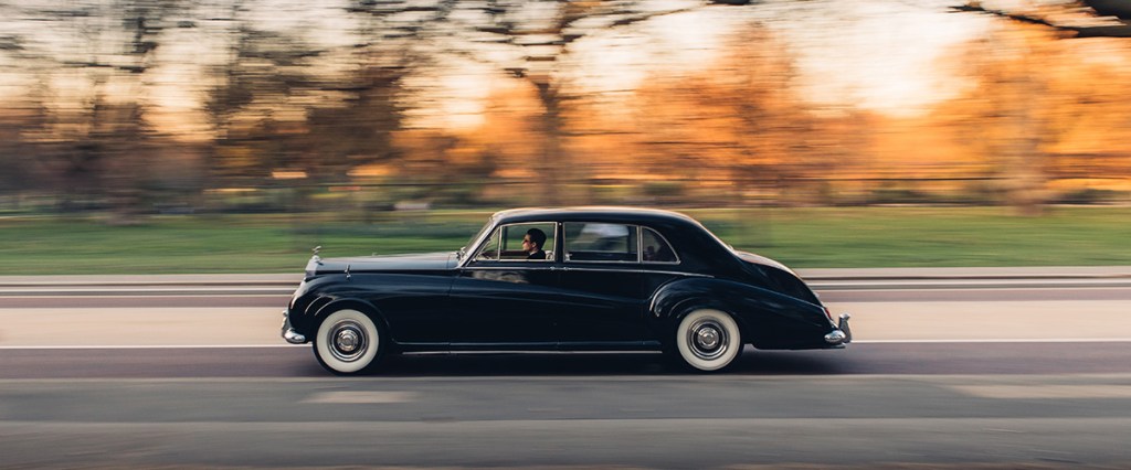 A black classic Rolls-Royce Phantom that has been converted to electric power is on the road at speed