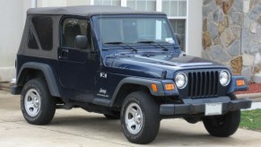 A blue 1990s Jeep Wrangler parked outside of a driveway.