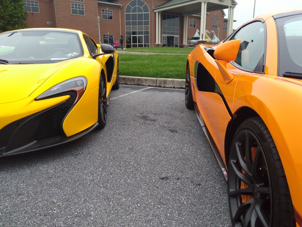 A yellow and orange McLaren sit side-by-side in a parking lot