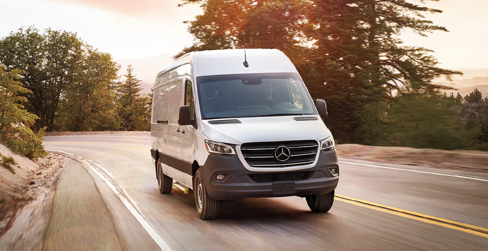 white Mercedes sprinter van driving down a forested road