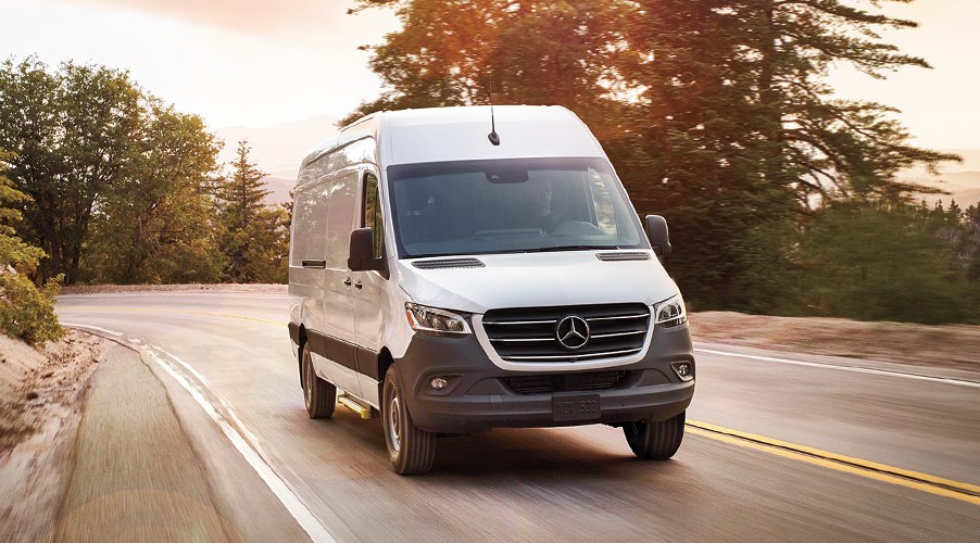 white Mercedes sprinter van driving down a forested road