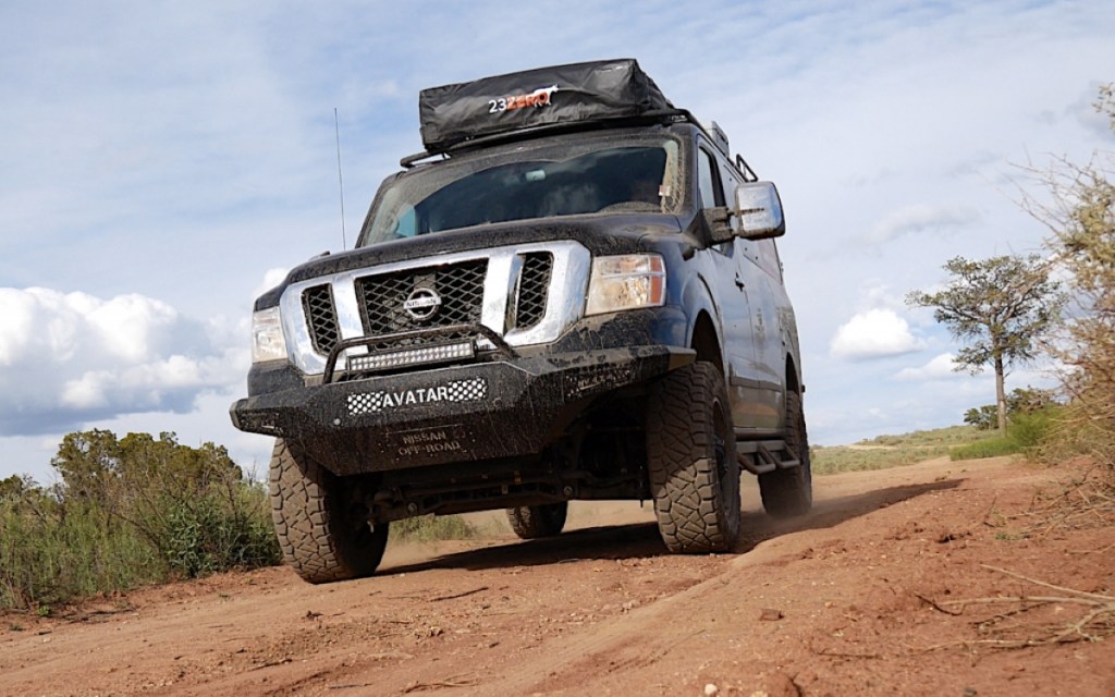 A black, lifted, 4x4, full-size van that has been converted for overlanding sits on a dirt road