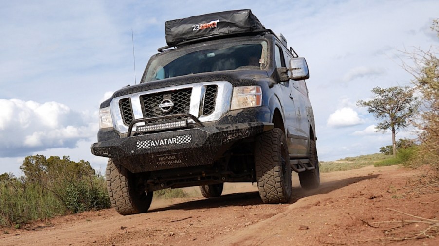 A black, lifted, 4x4, full-size van sits on a dirt road