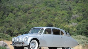 A silver 1941 Tatra T87 in front of a grassy hill