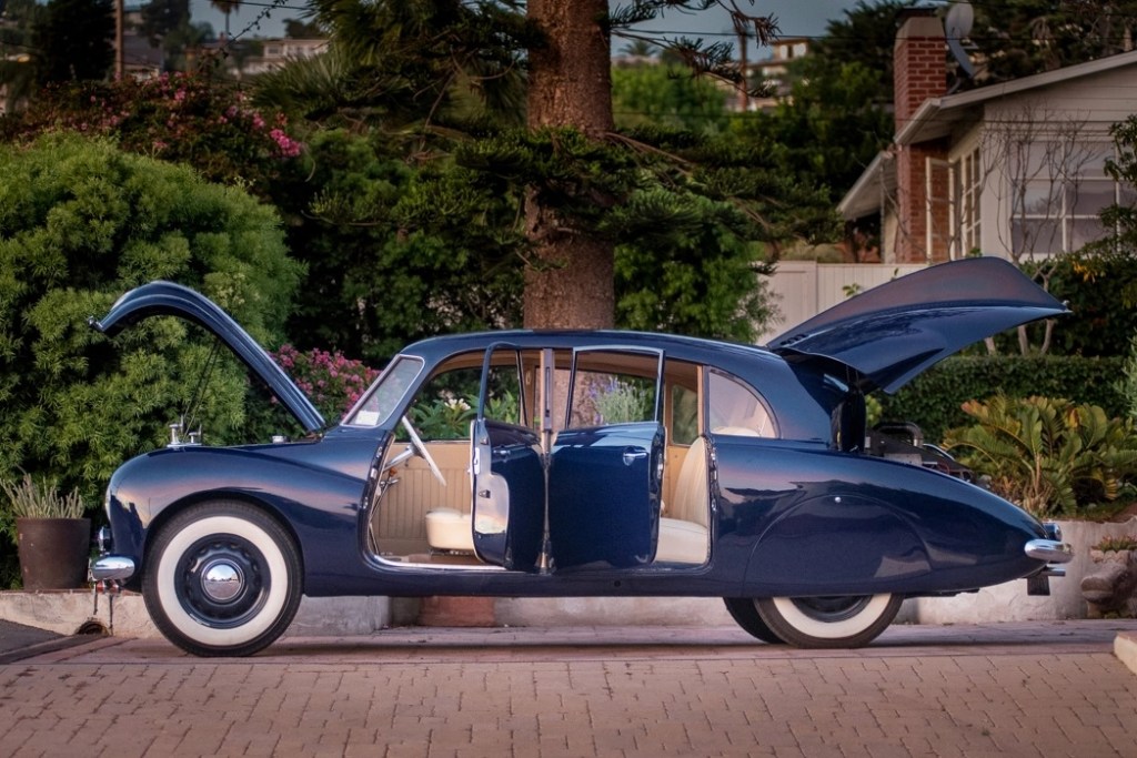 A side-view of a dark-blue 1950 Tatra T87, with its doors, front trunk, and rear engline-lid open