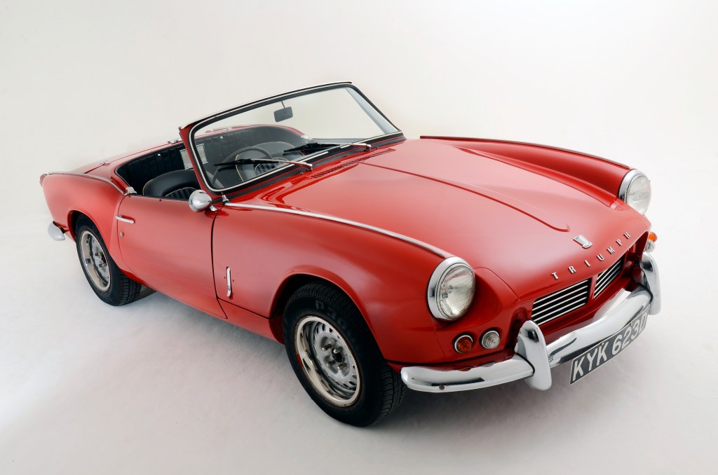 A red Triumph Spitfire convertible has its top down.
