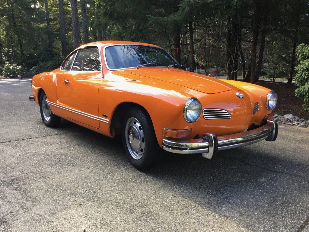 An orange 1972 Volkswagen Karmann Ghia coupe parked in a forest