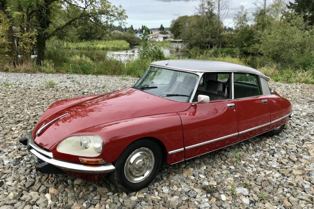 A red 1975 Citroen DS Pallas parked on a gravel forest road
