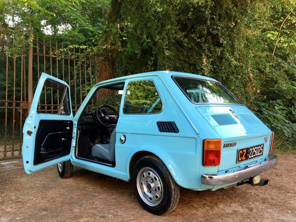 Rear view of a blue 1979 Fiat 126p, with its door open and showing some of the interior