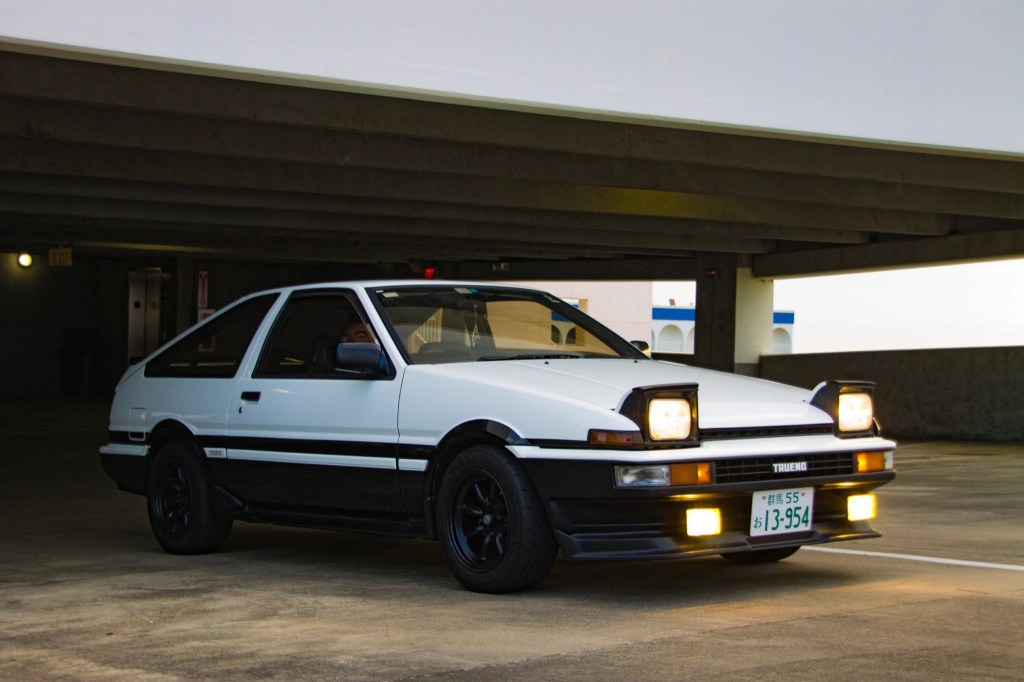 White 1986 Toyota AE86 Sprinter Truneo with headlights popped up, underneath a parking garage roof