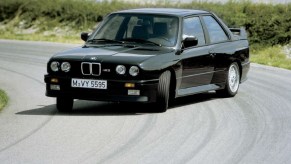 A black 1987 BMW E30 M3 drifting around a racetrack corner