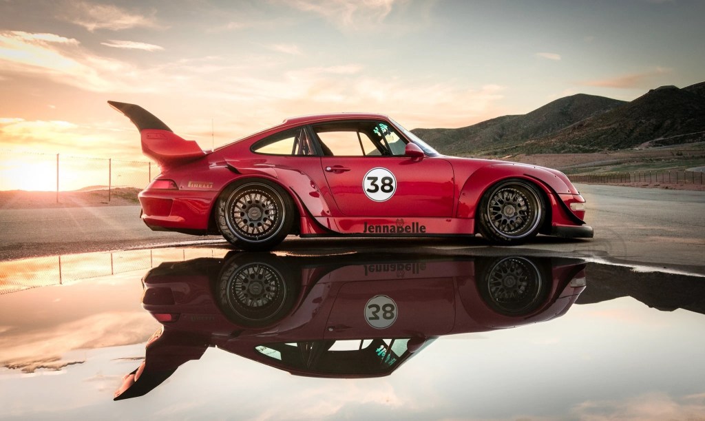 Side view of a red 1995 RWB Porsche 911 Carrera reflecting in a desert pool at sunset
