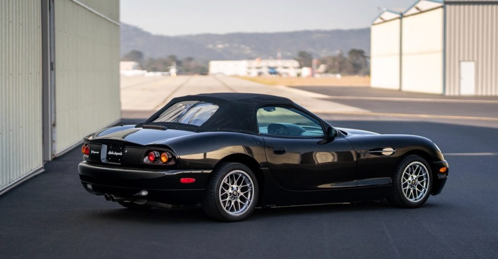 A rear shot of a black 2001 Panoz Esperante with the top up, next to some white storage units