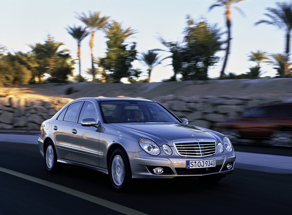 Silver 2006 Mercedes-Benz E-Class sedan driving down a road lined with palm trees