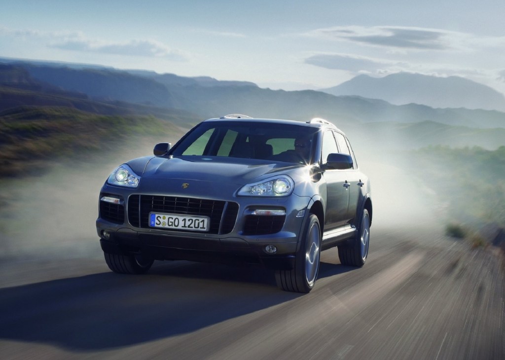 A silver 2008 Porsche Cayenne Turbo driving down a curving desert road, throwing up a plume of dust