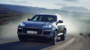 A silver 2008 Porsche Cayenne Turbo driving down a curving desert road, throwing up a plume of dust