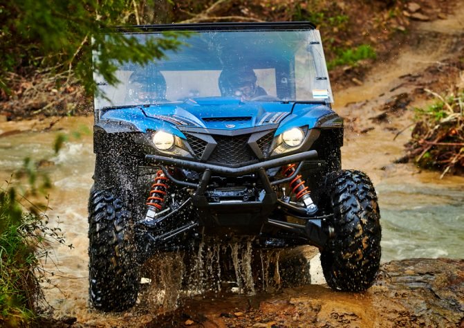 A blue Yamaha wolverine side-by-side crossing a muddy creek bed