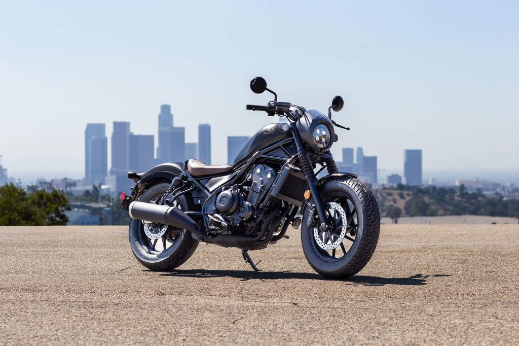 A brown-tanked 2020 Honda Rebel 500 cruiser parked with a city-scape in the distance